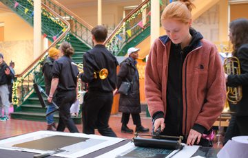 A person uses roller on a print in printmaking workshop.