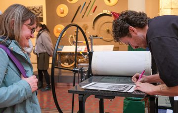 Artist signs print while a person watches.