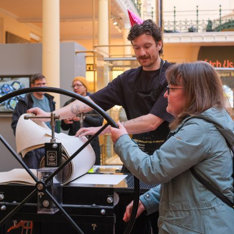 A person turning a wheel of a printing press in a demonstration.
