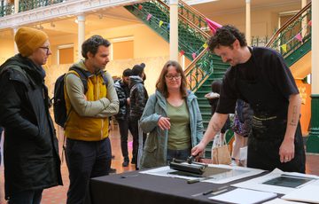People observe a person demonstrating printmaking.