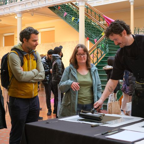 People observe a person demonstrating printmaking.