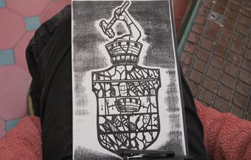 Hand holding a black-and-white print of a detailed shield.