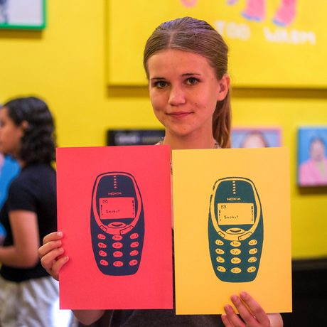 A person holds two colourful screen prints featuring mobile phones with different backgrounds.