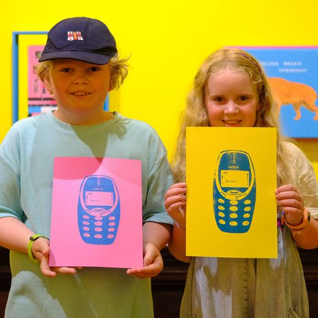 Two children hold colourful screen prints of mobile phones.