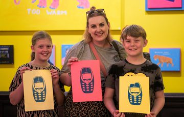 Three smiling people hold colourful prints of a mobile phone.