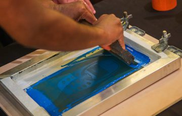 Hands spreading blue ink on a screen for silk screen printing process.