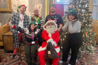 A group of staff dressed in festive jumpers and hats are next to Santa in a cafe.