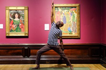 Man practices yoga pose between two framed paintings on a museum gallery wall.