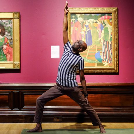 Man practices yoga pose between two framed paintings on a museum gallery wall.