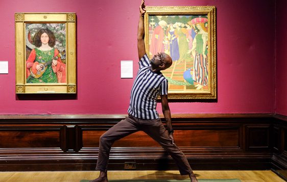 Man practices yoga pose between two framed paintings on a museum gallery wall.