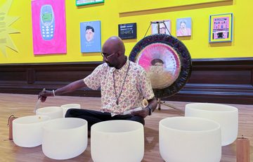 Man plays crystal bowls in a vibrant colourful art gallery with paintings on a yellow wall in background.