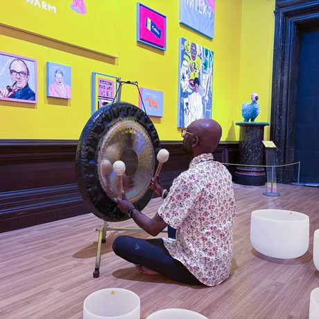 Man plays gong and crystal bowls in a vibrant colourful art gallery.