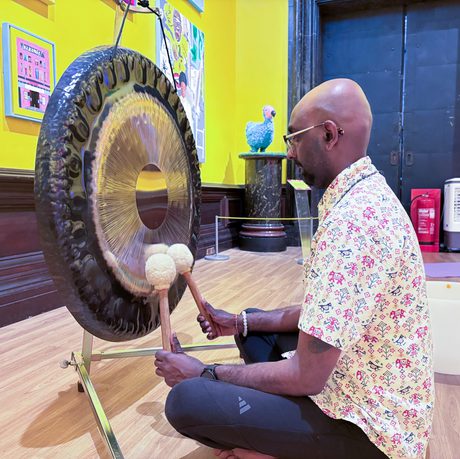 Man plays gong in vibrant colourful art gallery room.