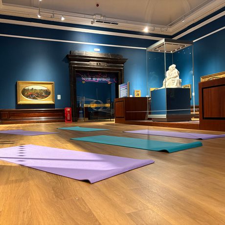Yoga mats laid out on the wooden floor of an art gallery with Pre-Raphaelite paintings and sculpture.