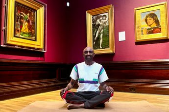 A person in a meditation yoga pose in an art gallery - paintings in gold frames are on the walls behind.