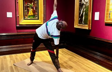 A person doing yoga in a art gallery - paintings in gold frames are on the walls behind.