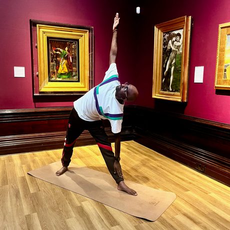 A person doing yoga in a art gallery - paintings in gold frames are on the walls behind.