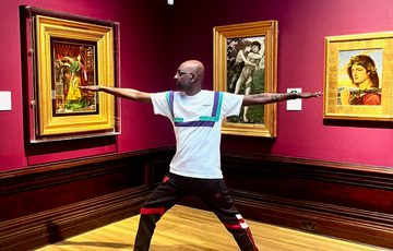 A person doing yoga in an art gallery - paintings in gold frames are on the walls.