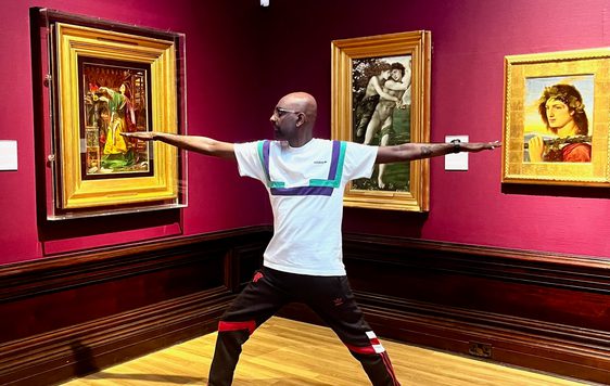 A person doing yoga in an art gallery - paintings in gold frames are on the walls.