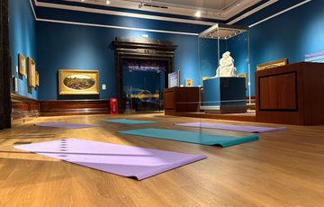 Yoga mats laid out on the wooden floor of an art gallery with Pre-Raphaelite paintings and sculpture.