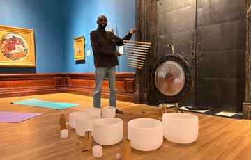 Man standing beside a gong and singing bowls in an art gallery room.