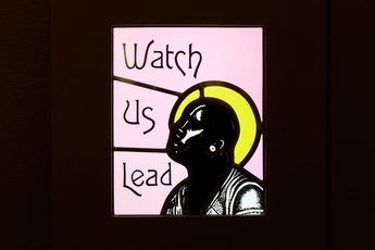 Close up of a stained glass with the text 'Watch Us Lead'.