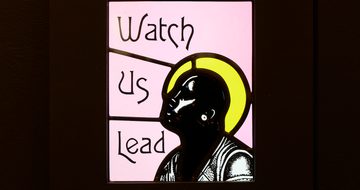 Close up of a stained glass with the text 'Watch Us Lead'.