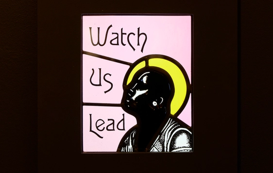 Close up of a stained glass with the text 'Watch Us Lead'.