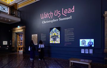 Display wall with people looking at the stained glass artwork.