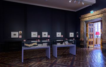 A gallery display with artwork on wall an display cases.