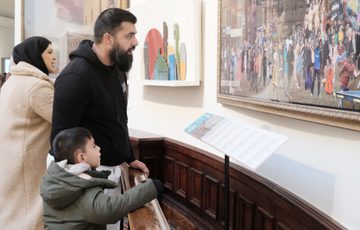 An adult and child looking at Benny's Babbies by Cold War Steve on display in the gallery.