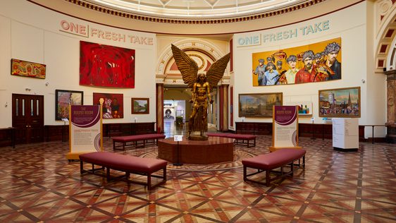 A view of the Round Room with large painting on the wall and a statue of Lucifer by Sir Jacob Epstein.