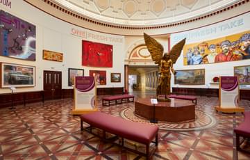 A view of the Round Room with large painting on the wall and a statue of Lucifer by Sir Jacob Epstein in the centre.
