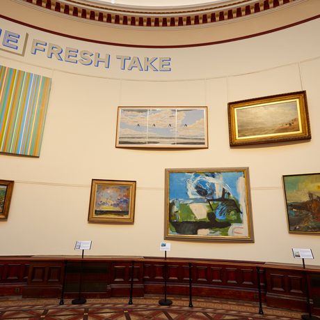 A group of paintings hanging on the wall of the Round Room with a title 'One Fresh Take'