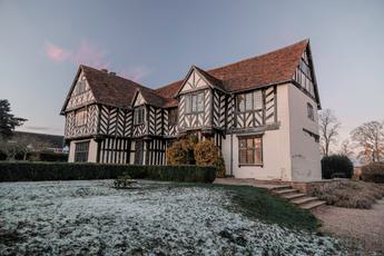 Exterior of Blakesley Hall, a Tudor house, at dusk with frost on the floor of the gardens.