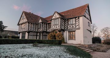 Exterior of Blakesley Hall, a Tudor house, at dusk with frost on the floor of the gardens.