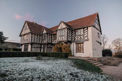 Exterior of Blakesley Hall, a Tudor house, at dusk with frost on the floor of the gardens.