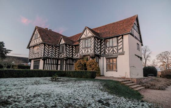 Exterior of Blakesley Hall, a Tudor house, at dusk with frost on the floor of the gardens.