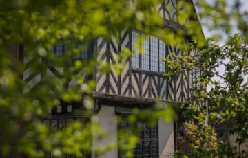 The front of Blakesley Hall obscured by the leaves of trees in front of it.