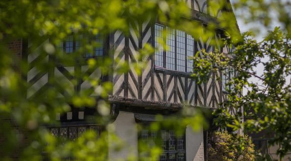 The front of Blakesley Hall obscured by the leaves of trees in front of it.