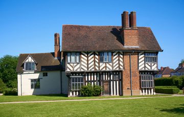 Exterior front view of a Tudor timber-framed house with chimney on the side.