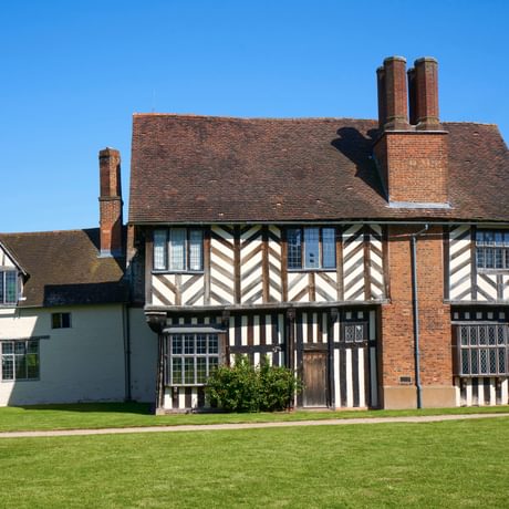 Exterior front view of a Tudor timber-framed house with chimney on the side.