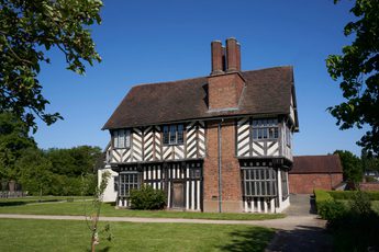 Exterior side view of a Tudor timber-framed house with large brick chimney on the side.
