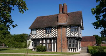 Exterior side view of a Tudor timber-framed house with large brick chimney on the side.