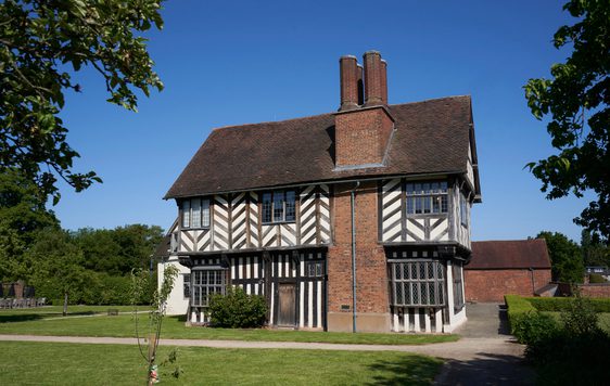 Exterior side view of a Tudor timber-framed house with large brick chimney on the side.