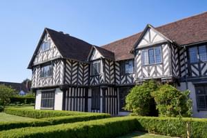 Exterior side view of the front of a Tudor timber-framed house and garden.