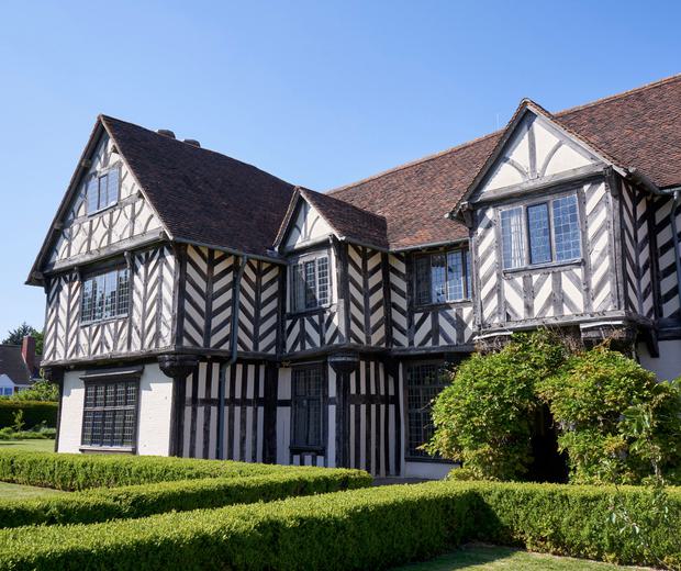 Exterior side view of the front of a Tudor timber-framed house and garden.