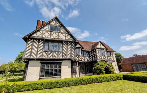 Exterior front view of a Tudor timber-framed house and garden.