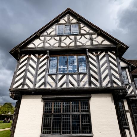 Exterior of Blakesley Hall showing a part of a black and white Tudor building with a dark cloudy sky