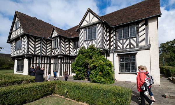 Exterior view of a Tudor timber-framed house with adults and children walking in the garden.